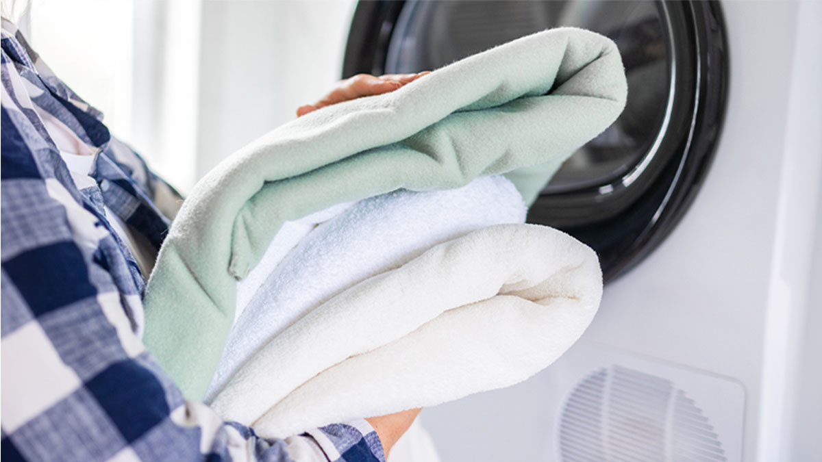 pessoa a segurar roupa lavada e dobrada em frente a máquina de secar roupa